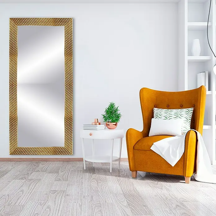 Espejo de pared Espiral - 56 x 150 cm, Oro - Un espejo rectangular con marco dorado texturizado apoyado contra una pared blanca, al lado de un sillón y una mesa auxiliar.
