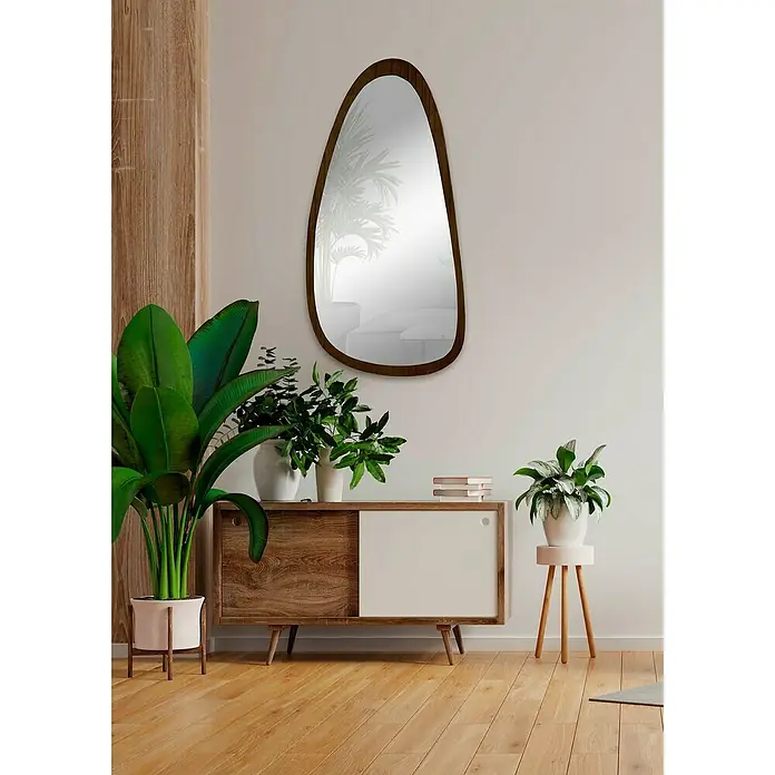 Espejo de pared Prisma - 58 x 118 cm, Tabaco - Un interior elegante con un espejo de forma orgánica con marco de madera que cuelga sobre un aparador con plantas.