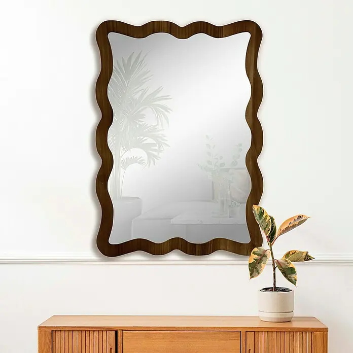 Espejo de pared Cube - 64 x 89 cm, Tabaco - Un espejo decorativo con un marco de madera ondulado cuelga sobre un armario de madera, destacando por su diseño.