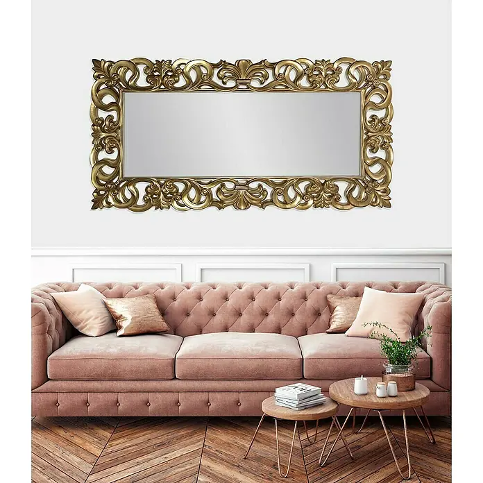 Espejo de pared Goya - 88 x 178 cm, Oro betún - Un espejo rectangular con un marco dorado ornamentado cuelga sobre un sofá rosa en una elegante sala de estar.