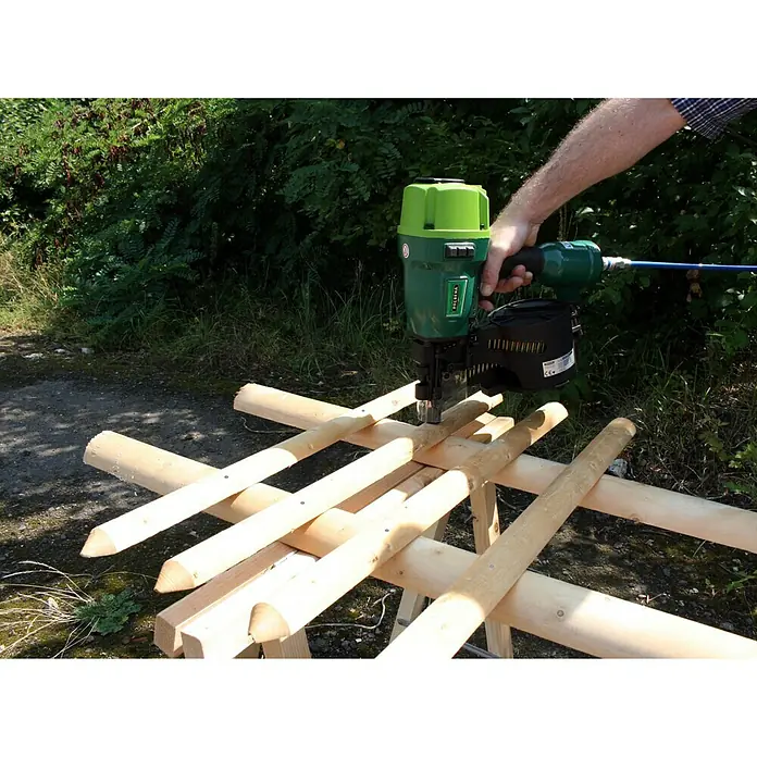 Prebena Druckluftnagler 8XR-CNW90 - Betriebsdruck: 5 bar - 8,3 bar, Passend für: Rundkopf-Coilnägel der Tye Typ CNW von 45 - 90 mm - Bild einer grünen Nagelmaschine der Marke VALENA im Einsatz beim Bau eines Holzzauns im Freien.