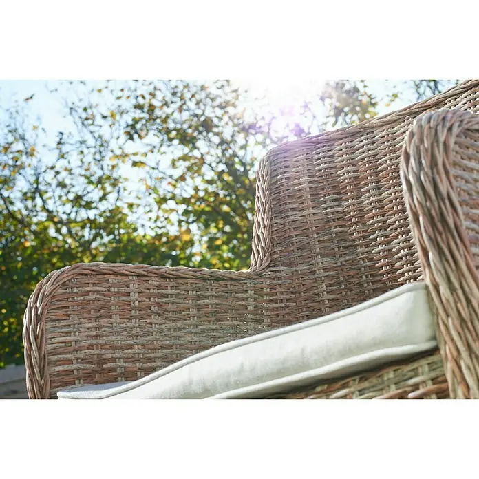 Sillón de jardín Gotland - An x Pr x Al: 79 x 63 x 99 cm, Arena - Primer plano de una silla de mimbre con cojín claro, con árboles y cielo azul al fondo.