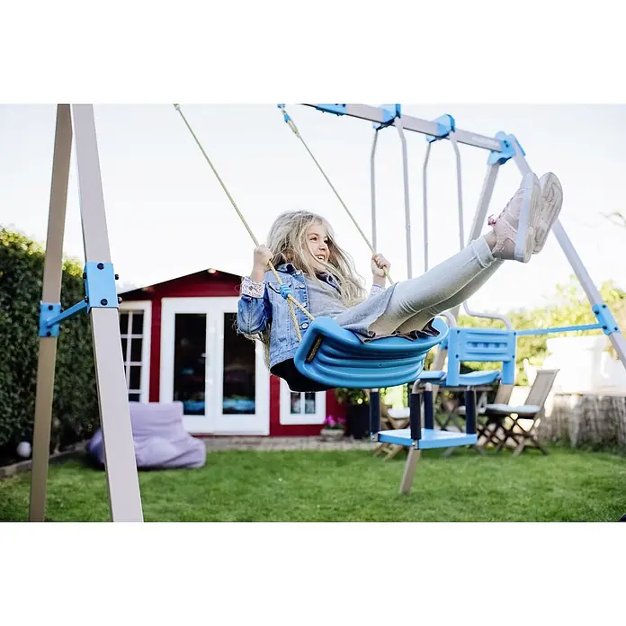 Hudora Schaukel Ergänzungsmodul Gondel - B x L: 40 x 89 cm, Stahl - Ein Mädchen schwingt auf einer blauen Schaukel im Garten. Die Schaukel ist Teil eines Spielsets mit weiteren Schaukeloptionen.