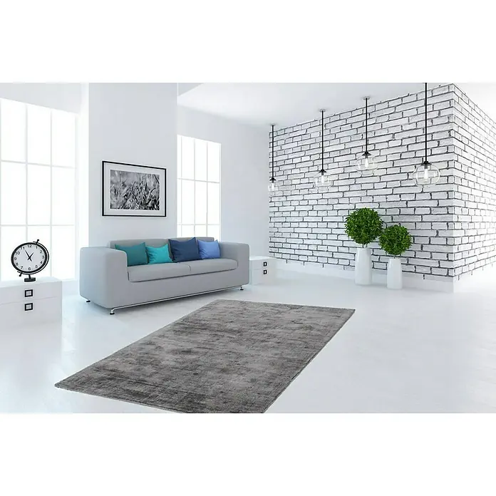 Kayoom Kurzflorteppich Luxury 110 - Grau, 150 x 80 cm, 100 % Viskose - Ein grauer Teppich liegt in einem modernen, minimalistischen Wohnzimmer mit weiß getünchten Wänden und Möbeln. Der Teppich ist das zentrale Element.