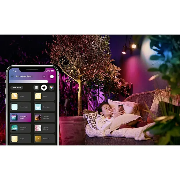Philips Hue LED-Gartenspot Lily - 8 W, Lichtfarbe: RGB, IP65 - Eine Frau entspannt im Hinterhof mit den smarten Philips Hue Lampen, die per App gesteuert werden und eine entspannende Atmosphäre schaffen.