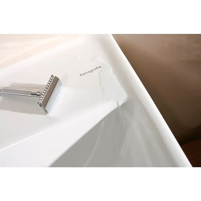 Hansgrohe Juego de lavabo Xanuia - 48 x 60 cm, Orificios para grifo: Medio, Con desbordamiento - Una elegante maquinilla de afeitar cromada reposa sobre un lavabo blanco, parcialmente cubierto de agua, realzando el brillo del metal.