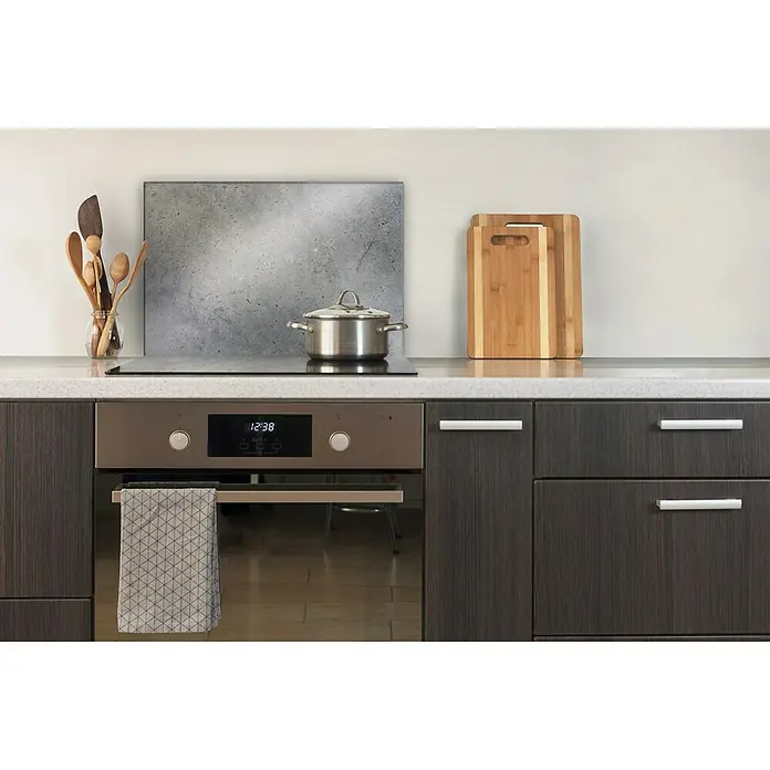 CUCINE Küchenrückwand - Dark Concrete, 60 x 40 cm, Stärke: 6 mm, Einscheibensicherheitsglas (ESG) - Nahaufnahme einer modernen Küche mit eingebautem Ofen, Kochfeld mit Topf, Holzlöffeln und Schneidebrettern.