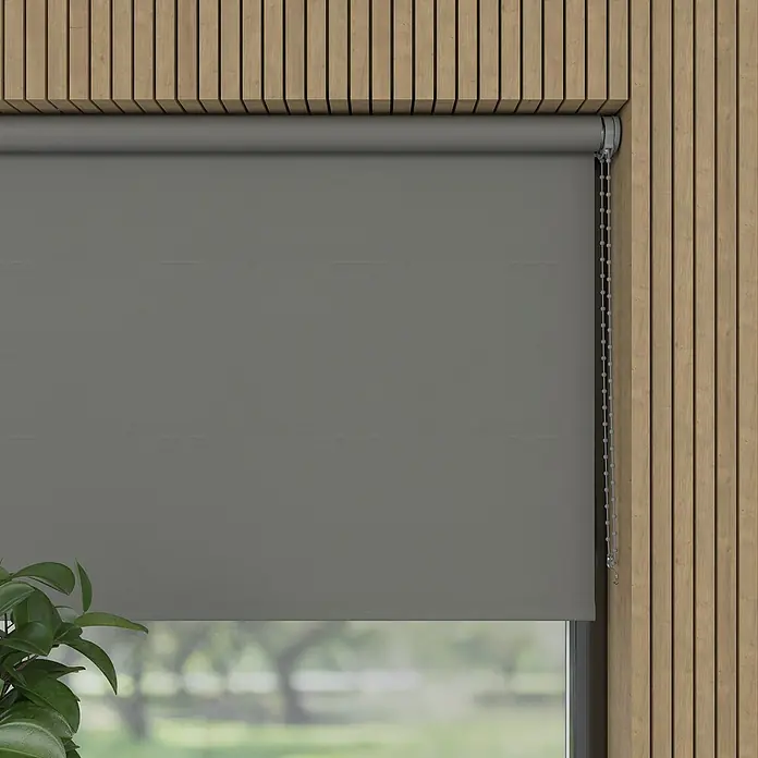 Verdunkelungsrollo - B x H: 130 x 190 cm, Metall, 100 % Polyester - Graue Rollläden mit Kettenzug vor einem Fenster mit Blick auf Bäume, montiert an einer Wand mit Holzpaneelen.