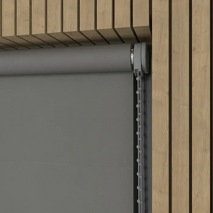 Verdunkelungsrollo - B x H: 130 x 190 cm, Metall, 100 % Polyester - Eine graue Rollo mit seitlichem Kettenzug ist vor einer hölzernen Wand angebracht. Ideal für moderne Wohnräume, bietet sie Privatsphäre und Schatten.