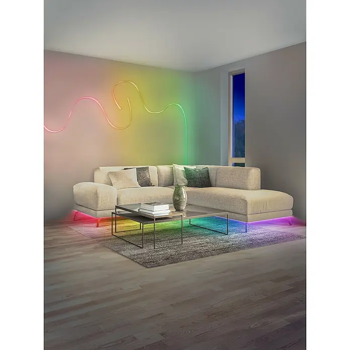 Osram Smart+ LED-Band Flex - Länge: 300 cm, Lichtfarbe: RGBW, 14 W, 1.500 lm, 220 V - 240 V - Ein modernes Wohnzimmer mit einem beigen Ecksofa, das mit farbigen LED-Leuchten unterlegt ist, und einer geschwungenen Lichtleiste an der Wand.