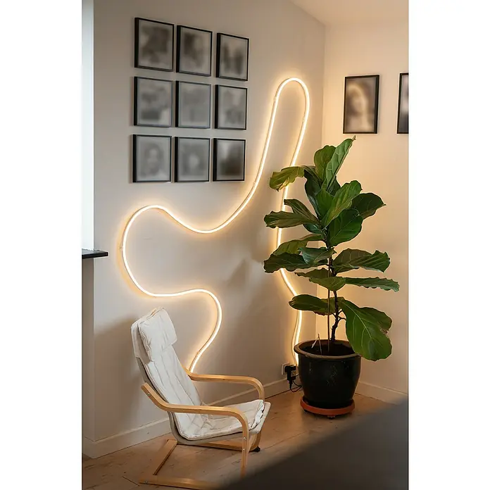 Ledvance LED-Stripes Smart WiFi Magic RGB Flex - Länge: 5 m, Lichtfarbe: RGB, 24 W - Ein stilvolles Interieur mit einem eleganten Stuhl und einer leuchtenden Neon-Wandleuchte, die eine warme Atmosphäre schafft.