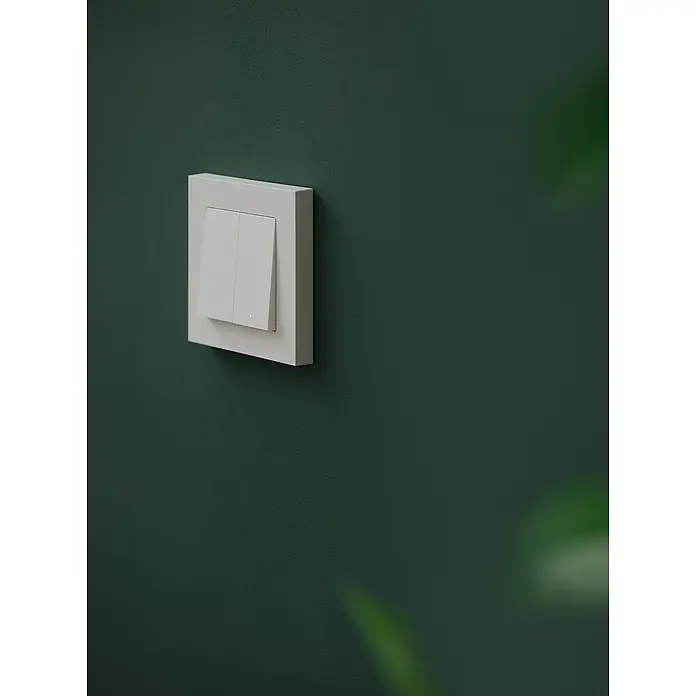 Osram Smart+ Schalter 2G matter - Weiß, Innen - Nahaufnahme eines weißen Lichtschalters an einer grünen Wand, der ein modernes und minimalistisches Design aufweist.