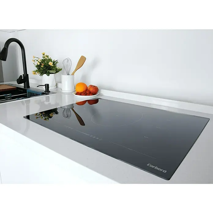 Corberó Placa de cocción CCIG5F800FZ - Número de fogones de inducción: 5 ud., 7.360 W - Primer plano de una placa de inducción Cerberó en una encimera de cocina, que muestra su diseño elegante y tecnología de cocina moderna.