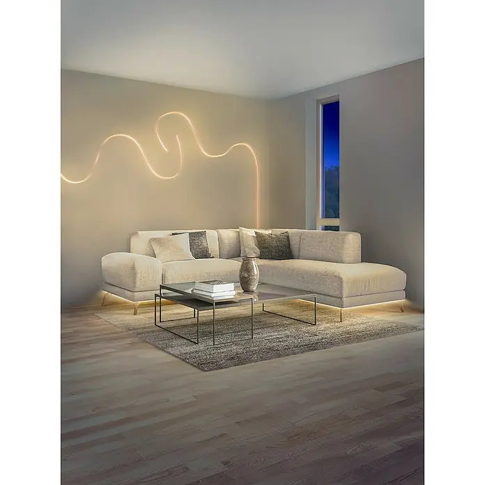 Osram Smart+ LED-Band Flex - Länge: 300 cm, Lichtfarbe: RGBW, 14 W, 1.500 lm, 220 V - 240 V - Elegantes Wohnzimmer mit beigem Sofa, Couchtisch und moderner Wandleuchte. Der Raum strahlt Gemütlichkeit und Stil aus.