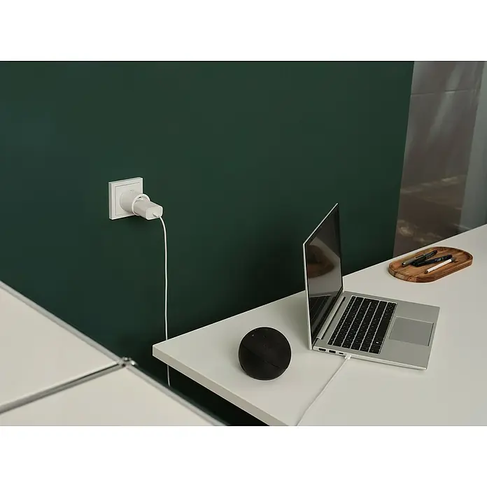Osram Smart+ Smart-Steckdose matter - Innen, Weiß, 2 Stk. - Nahaufnahme eines Laptops, eines smarten Lautsprechers und eines Ladegeräts an einer grünen Wand, die moderne Technologie und minimalistisches Design zeigt.