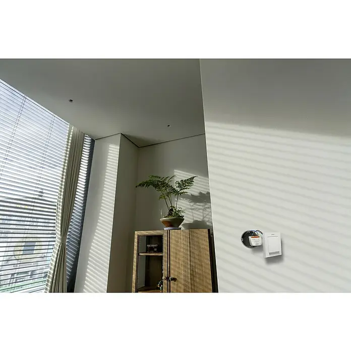 Osram Smart+ Schalter Vorhang - Weiß, Innen - Die Nahaufnahme zeigt einen montierten Lichtschalter an einer weißen Wand, der durch natürliches Licht betont wird, neben einem Holzschrank.