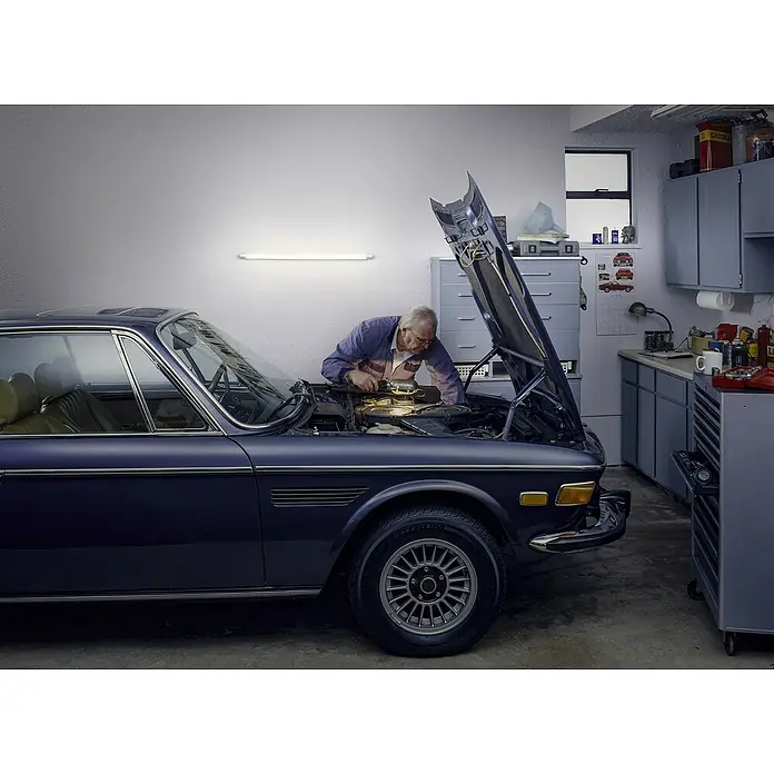 Osram LED-Lichtleiste Batten - L x B x H: 60 x 3,4 x 5,5 cm, Lichtfarbe: Kaltweiß, 8 W, 220 V - 240 V - Ein Oldtimer BMW wird in einer Garage repariert. Der Mechaniker ist konzentriert bei der Arbeit am Motor.