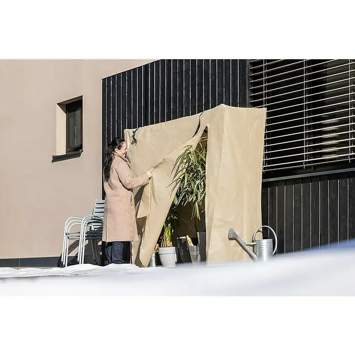 Windhager Winterschutzvlies Easy Up XXL - L x H: 200 x 180 cm, Beige, 100 g/m² - Eine Frau öffnet einen Winterschutz für Pflanzen. Der Schutz ist aus beigem Stoff und steht vor einer Hauswand.