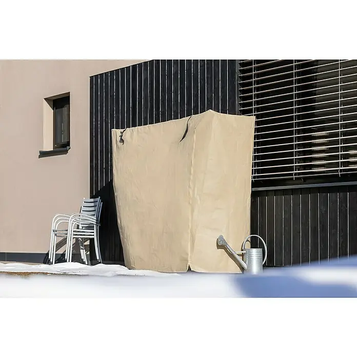 Windhager Winterschutzvlies Easy Up XXL - L x H: 200 x 180 cm, Beige, 100 g/m² - Ein beiger Schutzüberzug für Gartenmöbel steht draußen, neben einer Gießkanne, vor einem modernen Haus mit dunklen Holzdetails und schneebedecktem Boden.