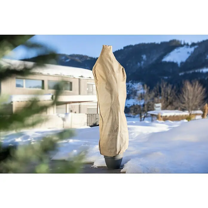 Windhager Winterschutzvlies - B x H: 60 x 180 cm, Beige, 50 g/m² - Diese Nahaufnahme zeigt eine Pflanze in einem Topf, die mit einer beigen Frostschutzhülle vor dem Winter geschützt ist, im Freien mit Schnee.