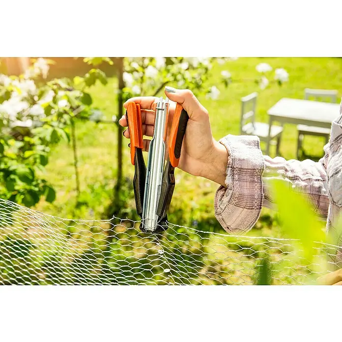 Windhager C-Ring-Zange - Passend für: C-Drahtringe - Eine Hand hält eine Drahtklammer-Zange, um ein Drahtgeflecht im Garten zu befestigen. Das Werkzeug hat orangefarbene Griffe.