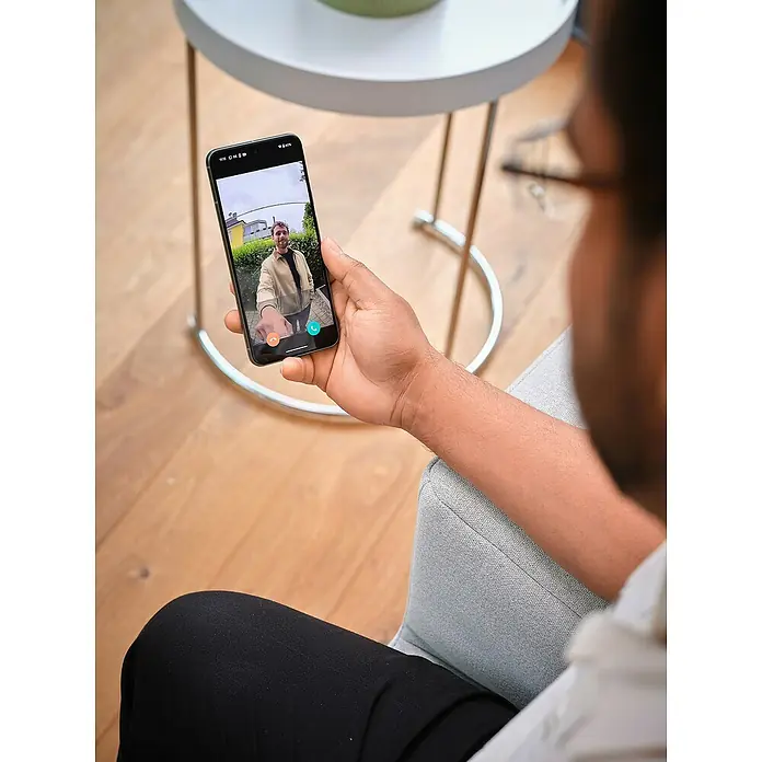 Osram Smart+ Türklingel mit Kamera - Weiß - Person hält ein Smartphone mit Videoanruf in der Hand. Der Fokus liegt auf dem Handy-Display und der Interaktion mit dem Gerät.