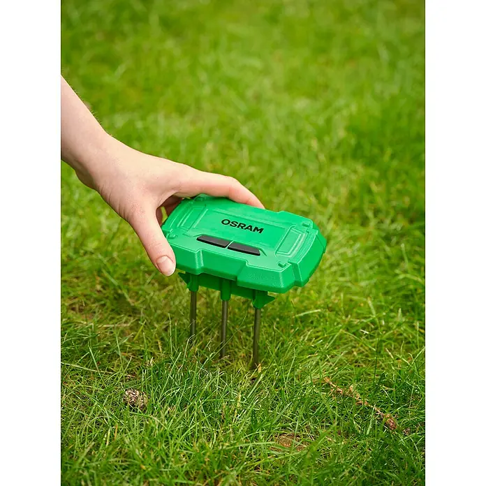 Osram Smart+ Bodenfeuchtesensor - Grün - Ein grüner Osram Gartenstecker wird in einen grünen Rasen gesteckt. Er dient als Stromquelle für Gartengeräte.