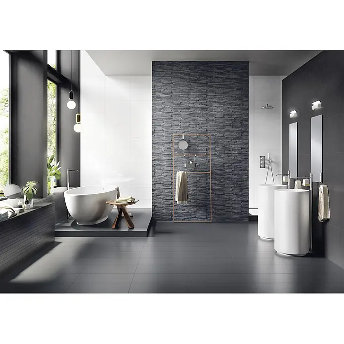 Ambiente by Palazzo Feinsteinzeugfliese - 30 x 60 cm, Schwarz, Matt - Badezimmer mit freistehender Badewanne, Waschtischen und dunklem Steinwand-Design. Die Armaturen sind modern gestaltet.