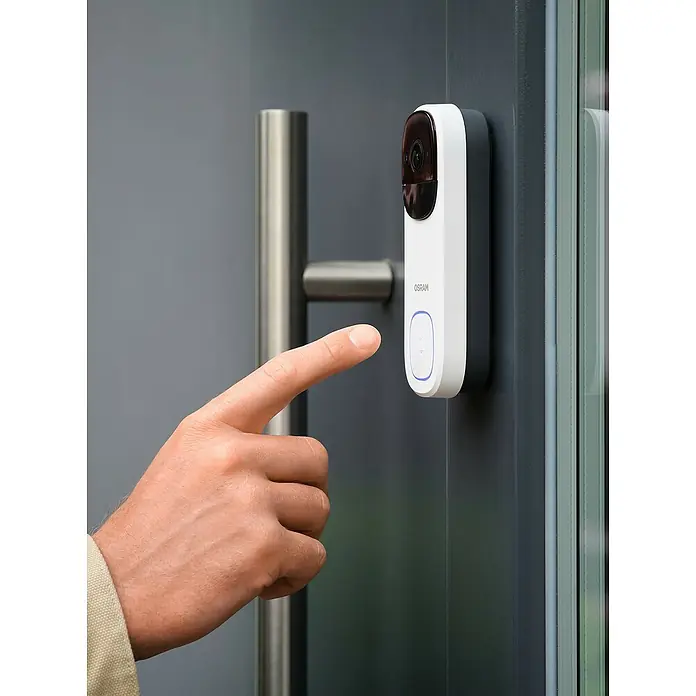 Osram Smart+ Türklingel mit Kamera - Weiß - Finger drückt die Taste an einer smarten OSRAM Türglocke mit Kamera, die an einer modernen Tür befestigt ist.