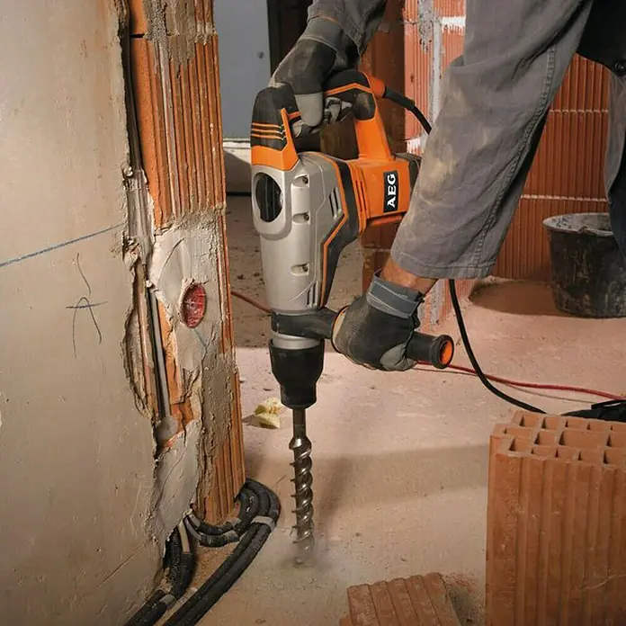 AEG Powertools Kombihammer KH 5 G - 1.100 W, 7,5 J, SDS-Max-Aufnahme - Nahaufnahme einer AEG Bohrmaschine im Einsatz auf einer Baustelle, die ein Loch in eine Wand bohrt.\n