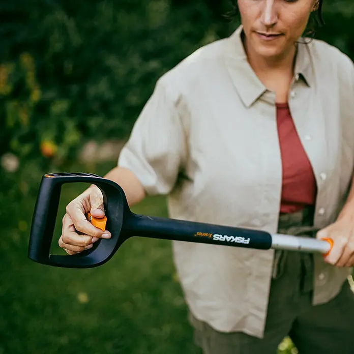 Fiskars X-series Unkrautstecher - Länge: 1.100,7 mm - Frau bedient einen Fiskars X-Series Unkrautstecher im Garten, wobei der Griff und die verstellbare Teleskopstange hervorgehoben werden.