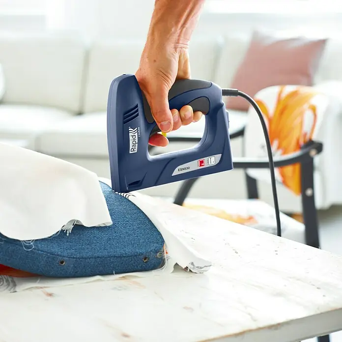 Rapid Kombi-Elektrotacker ESN530 - Klammertiefe: 6 mm - 14 mm, Elektrisch - Eine Person benutzt einen blauen Rapid ESN530 Elektrotacker, um einen Stoff an einem Möbelstück zu befestigen.