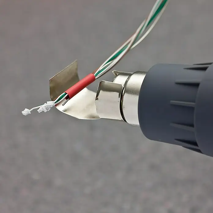Rapid Schrumpfschlauch-Set - Durchmesser: 3 mm - 12 mm, 36 -tlg. - Nahaufnahme einer Heißluftpistole, die zum Schrumpfen von Schrumpfschläuchen auf Drähten verwendet wird. Ideal für Elektroarbeiten und Reparaturen.