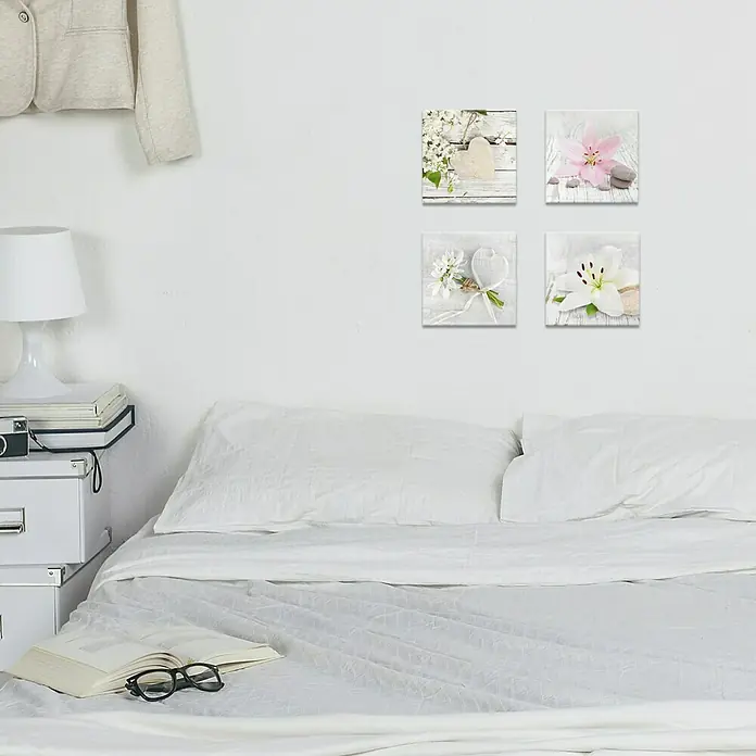 Glasbild - White Spring I, B x H: 20 x 20 cm - Eine Nahaufnahme von vier weißen Blumenkunstwerken, die über einem Bett in einem hellen Raum hängen. Die Kunstwerke sind quadratisch und zeigen verschiedene Blumenmotive.