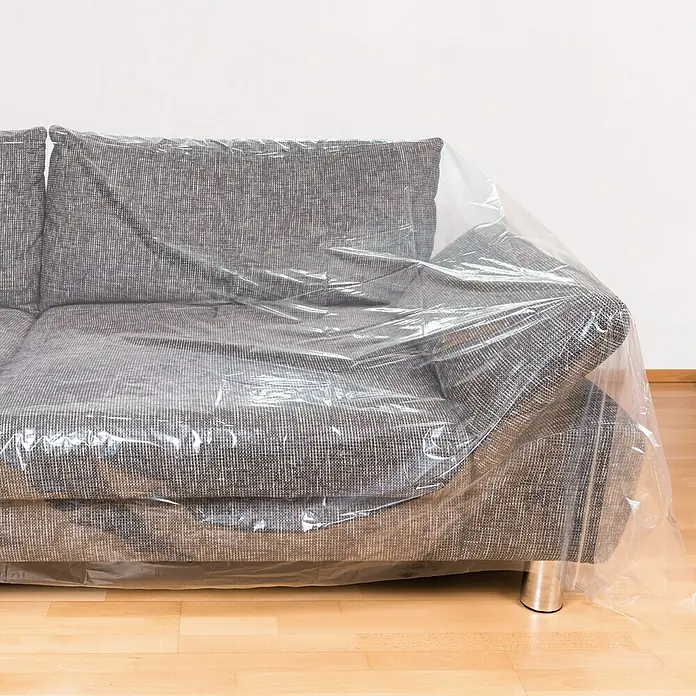 Couchhülle - 300 x 130 cm, Transparent, 2 Stk. - Ein graues Sofa ist mit einer durchsichtigen Plastikschutzhülle abgedeckt, um es vor Staub und Schmutz zu schützen. Die Hülle bedeckt das gesamte Möbelstück.