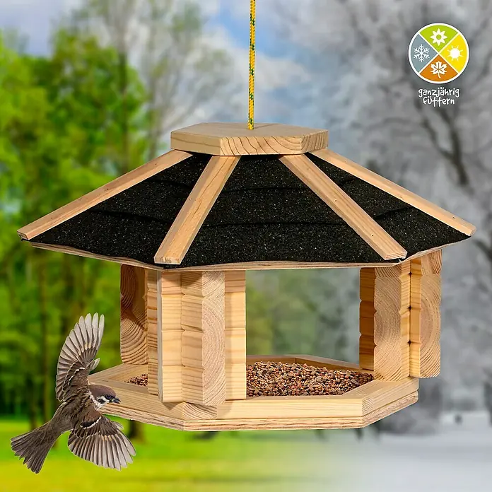 Dobar Vogelhaus Zwart - Holz, Natur/Schwarz - Holz-Vogelhaus mit Saatgut und fliegendem Vogel davor. Geeignet für die ganzjährige Fütterung von Vögeln im Garten.