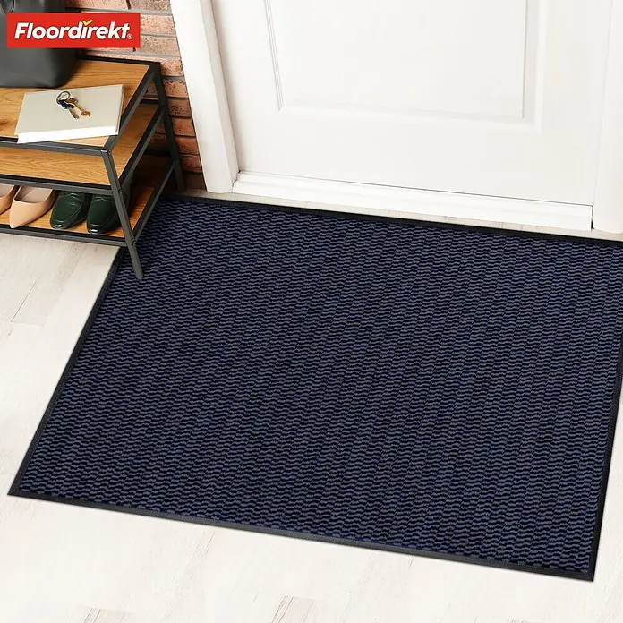 Fußmatte Sky Novo - Blau, 120 x 80 cm, Material Nutzschicht: 100 % Polypropylen - Eine dunkelblaue Fußmatte mit einem gewellten Muster, die vor einer weißen Tür auf einem hellen Boden liegt.