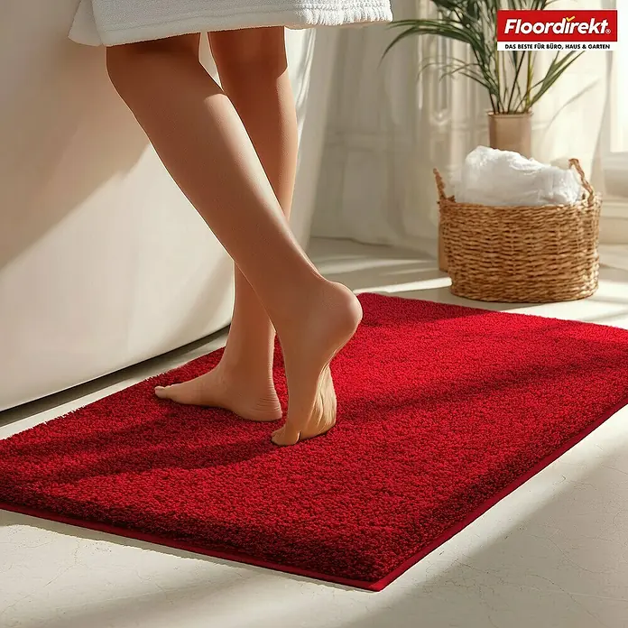 Badteppich Nasa - 50 x 80 cm, Rot, 100% Polyester - Roter Badteppich vor Badewanne mit Person in Handtuch.