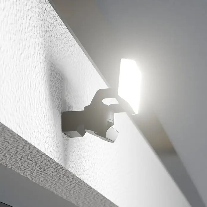 Steinel LED-Sensor-Außenwandleuchte XLED Protect S - 14,3 W, Anthrazit, Warmweiß - Nahaufnahme einer hell leuchtenden LED-Sicherheitsleuchte, die an einer strukturierten Außenwand montiert ist und für verbesserte Sicherheit sorgt.