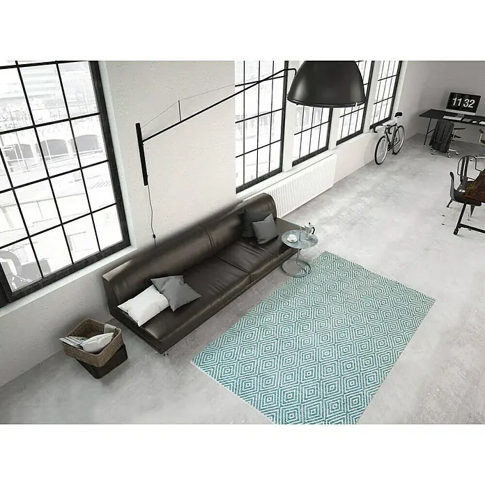 Kayoom Flachgewebeteppich Cocktail 300Türkis, 150 x 80 cm, 100% Baumwolle - Ein Wohnzimmer mit einem türkisfarbenen Teppich mit geometrischem Muster, einer Couch und großen Fenstern.
