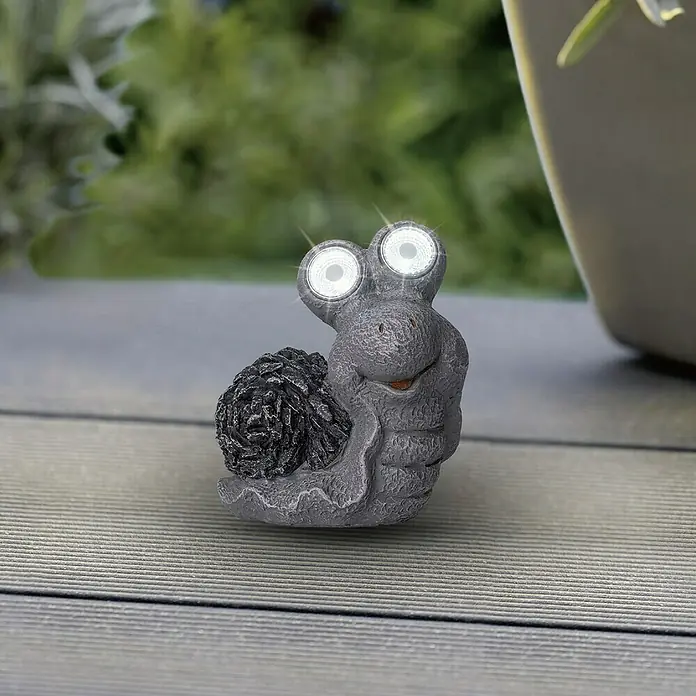 BAUHAUS Solar-Dekoleuchte Mini - LED, Grau, IP44, Schnecke - Eine graue Schnecken-Gartenleuchte mit großen, leuchtenden Augen steht auf einer Holzterrasse. Die Solarleuchte ist ein Hingucker im Garten.