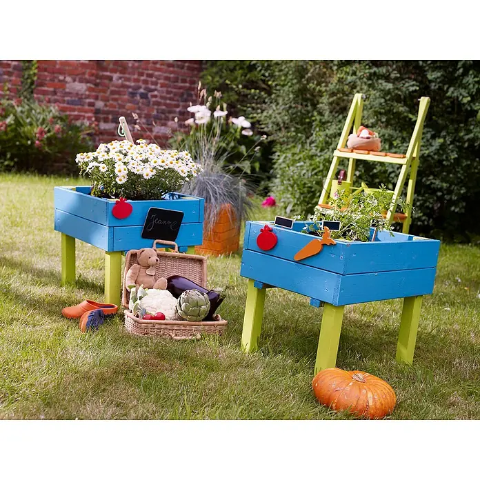 Soulet Hochbeet Lernbeet Marguerite - 40 x 50 x 45 cm, Holz, Natur - Kreative Gartenszene mit blauen Pflanzkästen auf hellgrünen Beinen, umgeben von Gemüse, Blumen und Gartengeräten.