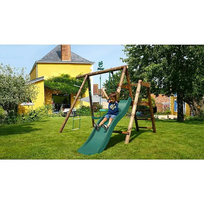 Soulet Schaukel Murier - B x L: 283 x 243 cm, Holz - Ein Kind saust auf einer grünen Rutsche einer hölzernen Schaukelanlage im Garten hinunter, umgeben von grüner Natur und einem gelben Haus.