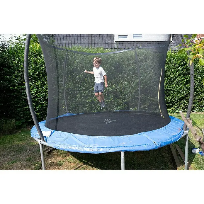 Soulet Trampolin - Ø x H: 366 x 260 cm - Ein Junge springt auf einem blauen Trampolin mit Sicherheitsnetz. Das Trampolin steht im Garten vor grünen Büschen und einem Haus.