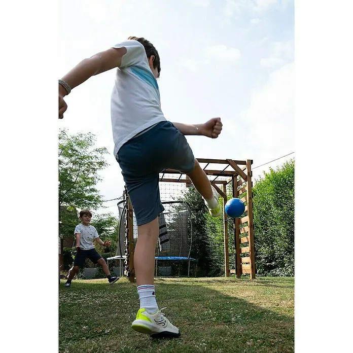 Soulet Kinderspielturm Olympic Odin - L x B x H: 216 x 153 x 209 cm - Ein Junge tritt einen blauen Ball vor einer hölzernen Torstruktur im Garten, während ein anderer Junge zusieht.