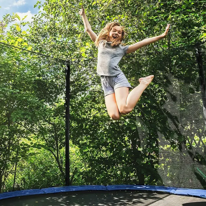 Soulet Trampolin - Ø x H: 366 x 260 cm - Fröhliches junges Mädchen springt hoch auf einem Trampolin, umgeben von üppigem Grün.