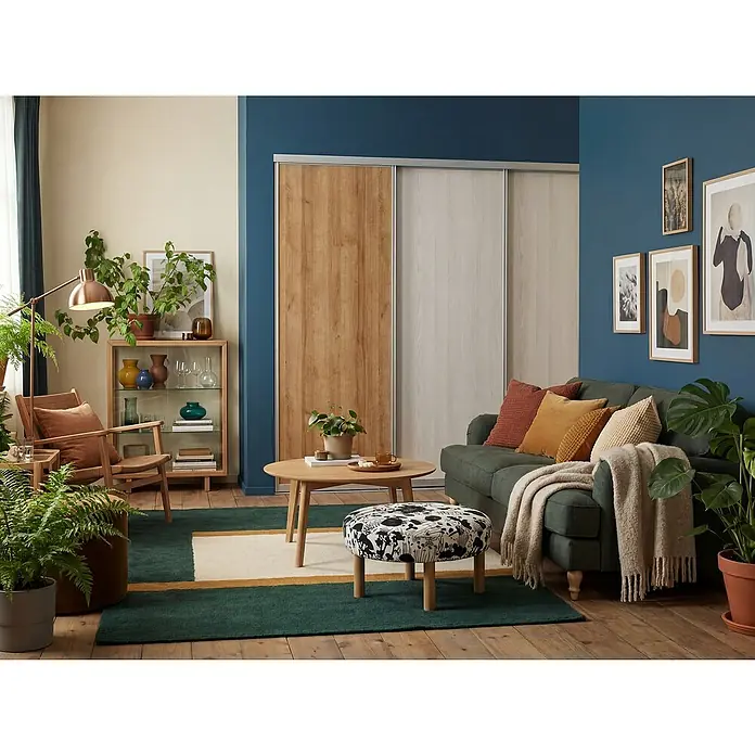 Room Plaza Easy Schiebetür-Bau-Set - Eiche Country/Pinie White, Farbe Beschlag: Silber - Ein gemütliches Wohnzimmer mit einem grünen Sofa, einem runden Tisch und einem Schrank mit Schiebetüren, das eine entspannende Atmosphäre schafft.
