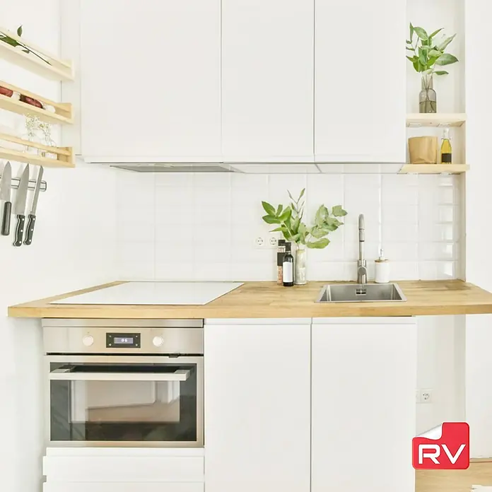Lámina decorativa autoadhesiva vinílico autoadhesivo a metros - Blanco soft - Una zona de cocina luminosa con armarios blancos, una encimera de madera, un fregadero de acero inoxidable y un horno moderno.