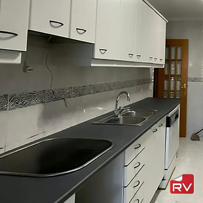 Lámina decorativa autoadhesiva vinílico autoadhesivo a metros - Piedra oscura - Detalles de cocina con armarios blancos, una encimera oscura, fregadero y vitrocerámica. Diseño elegante de cocina centrado en la funcionalidad y la estética.