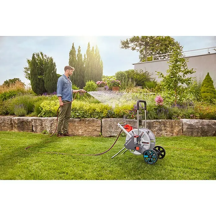 Gardena Schlauchwagen AquaRoll M Metall - Kunststoff/Metall, Schlauchkapazität: 60 m, 13 mm (½″) - Ein Mann bewässert seinen Garten mit einer grauen Gardena Schlauchtrommel mit Rädern, die für Komfort und einfache Handhabung sorgt.